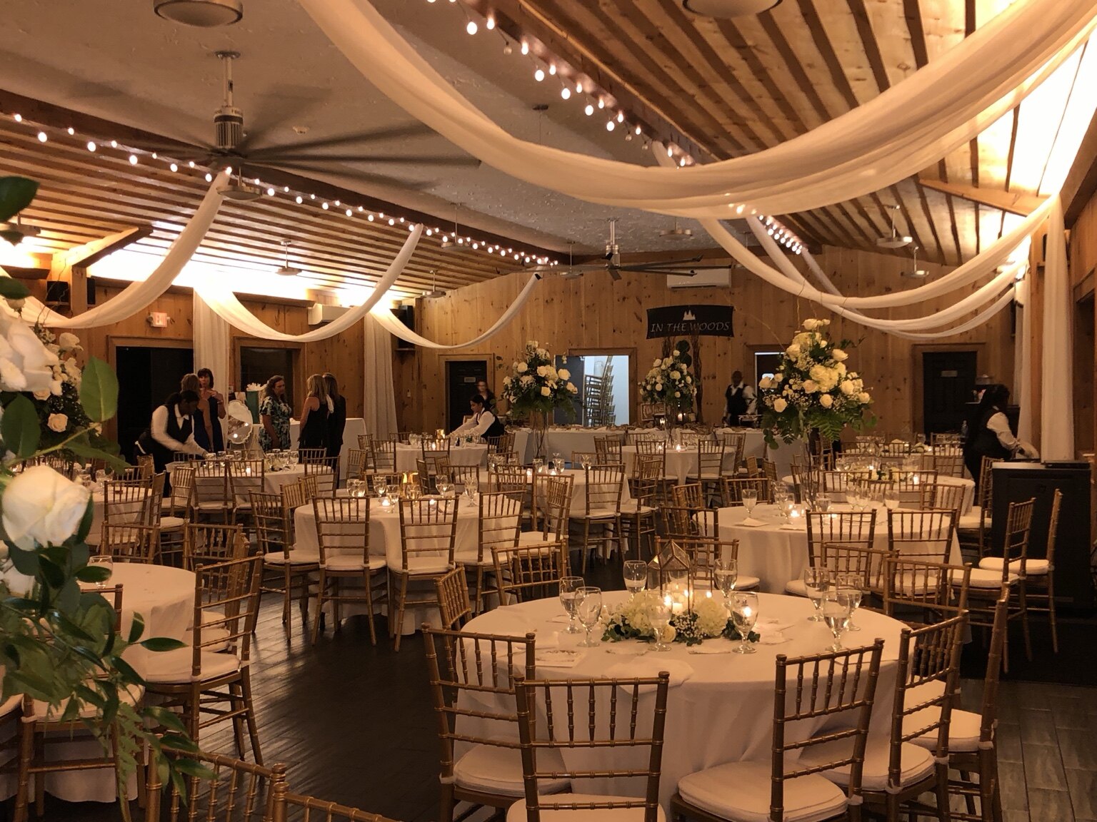 Elegant candlelit event room with draped ceilings, floral arrangements and gold chairs