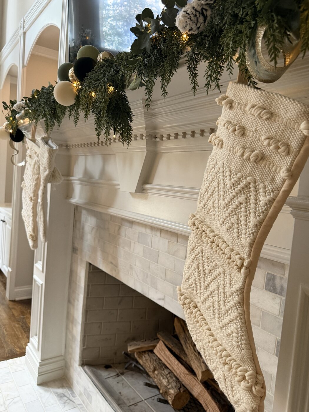 Christmas mantel with cascading greenery, warm lights and ivory stockings