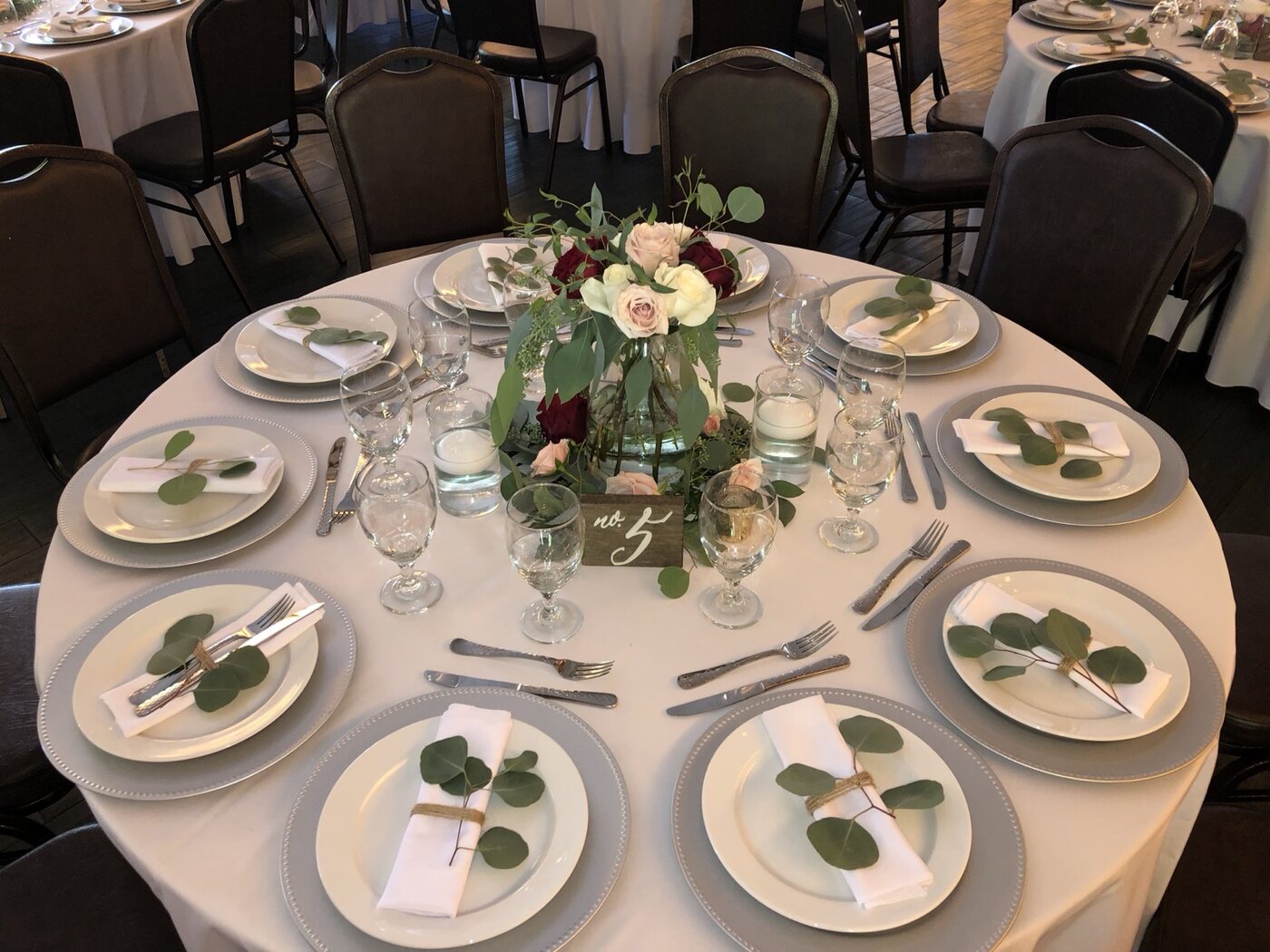 Round table with eucalyptus place settings, candlelight and rose centerpiece